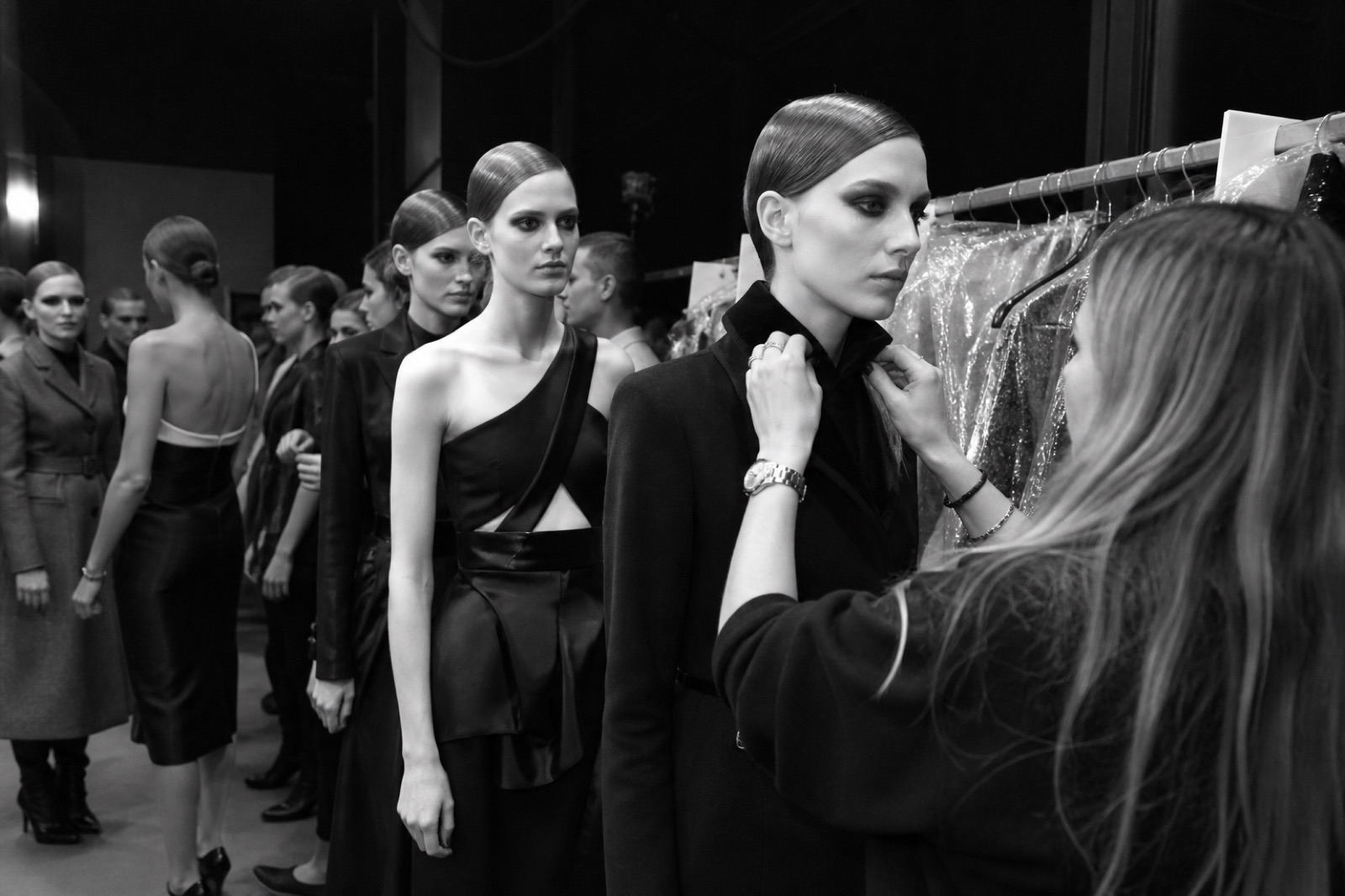 Black-and-white backstage scene at a fashion show with models and a stylist
